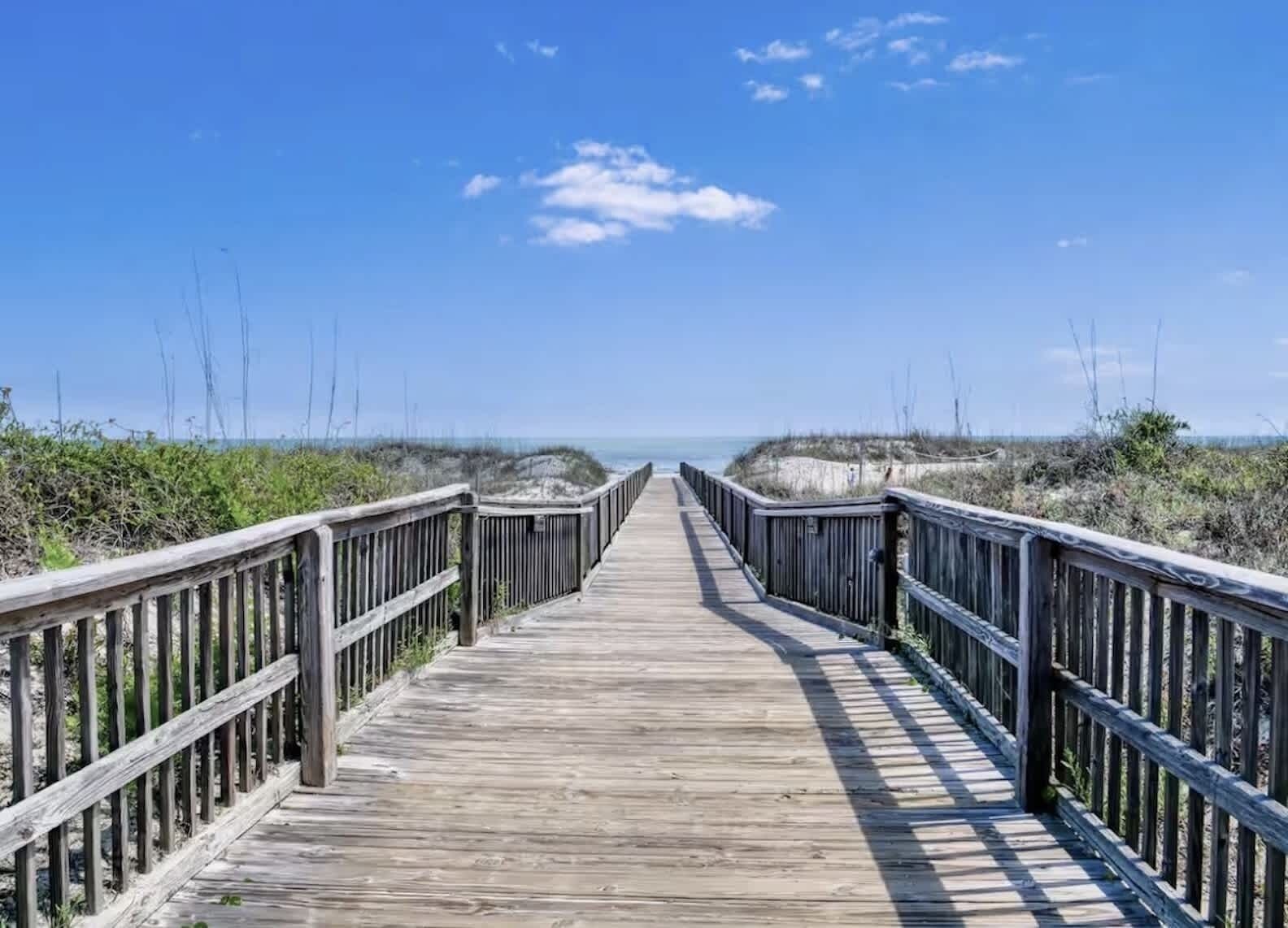A wooden boardwalk leading to the beach with a clear sky.