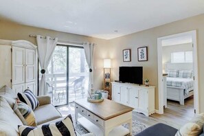 A room with a sofa, a table, a TV, a cabinet, and a bed. - Inviting Coastal Villa Short Walk to the Beach (Hilton Head)