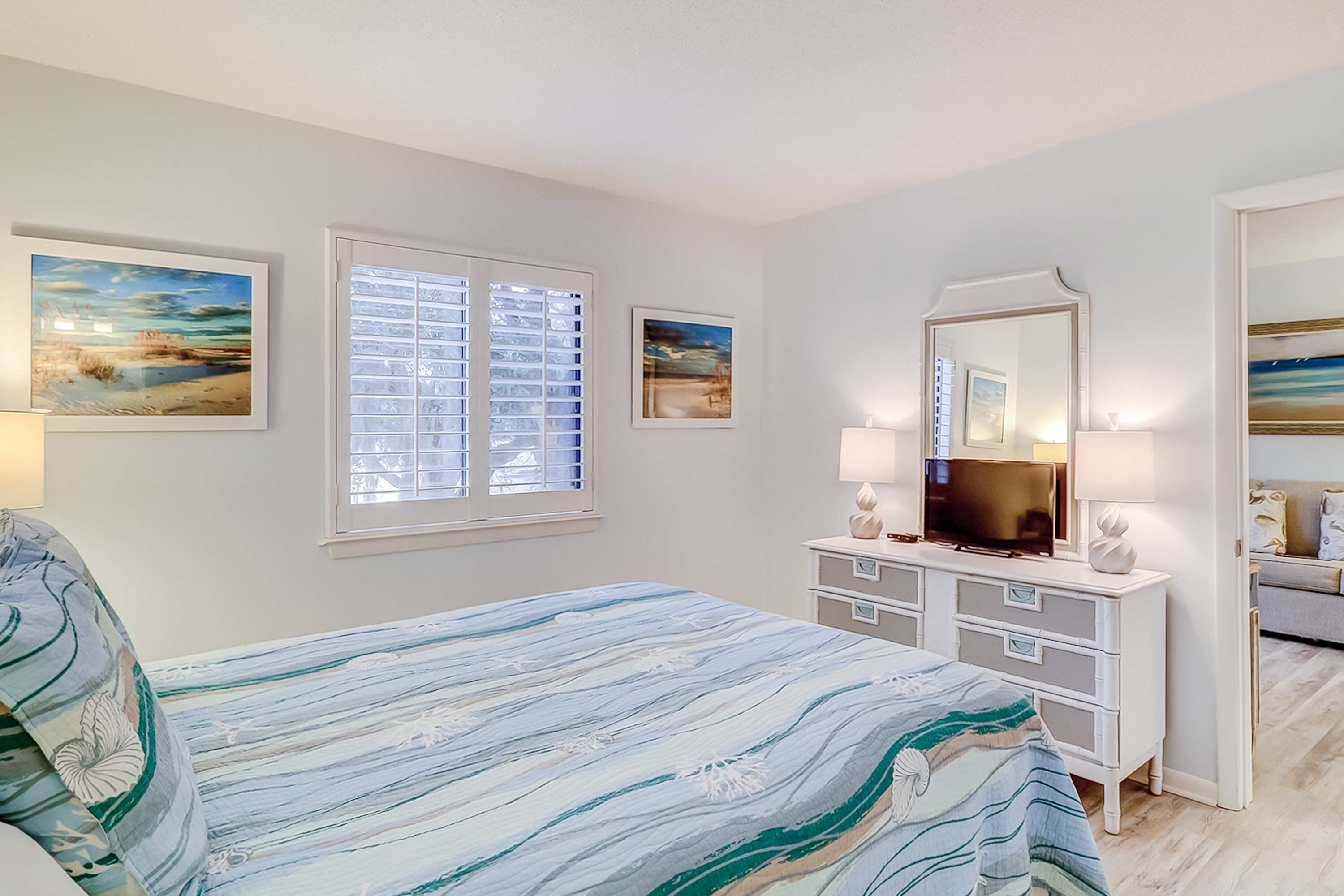 Une chambre à coucher avec un lit, une commode, un téléviseur et des œuvres d’art accrochées aux murs.