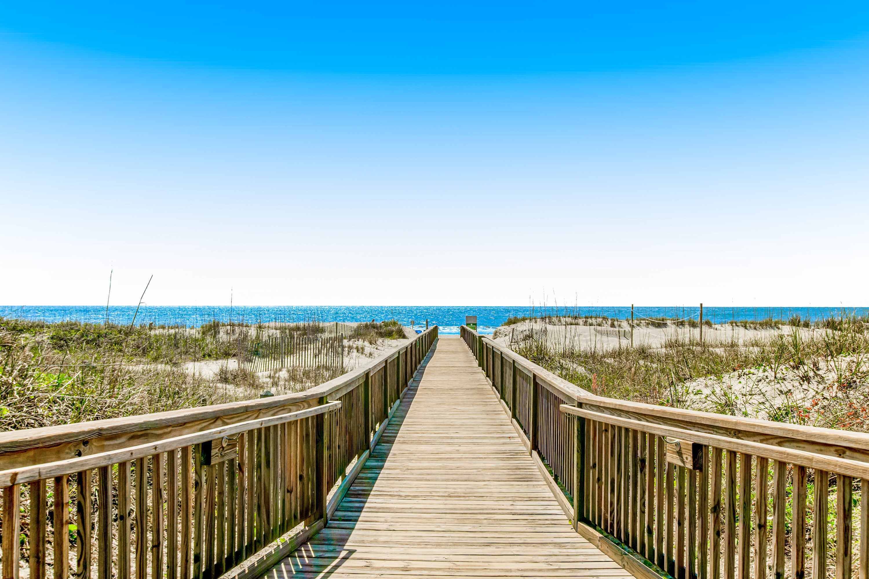 A wooden boardwalk leading to a beach with clear skies.