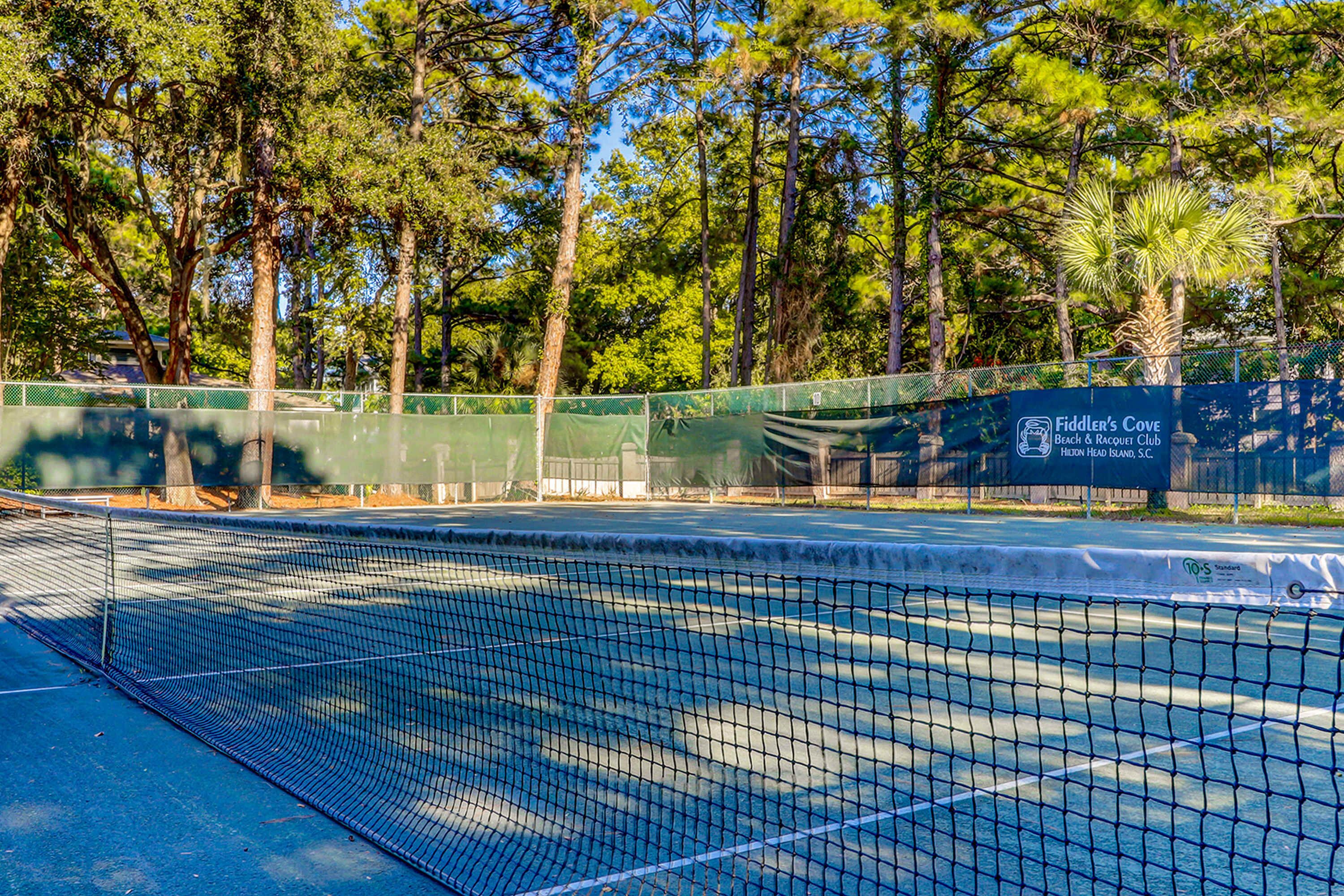 Ein Tennisplatz mit Netz, umgeben von Bäumen und einem Zaun.