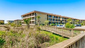 A multi-story hotel with balconies, a parking area, and a wooden boardwalk. - Coastal Condo with Pool, Hot Tub, Tennis, Fast WiFi, AC, & WD, Near the Beach (Hilton Head)