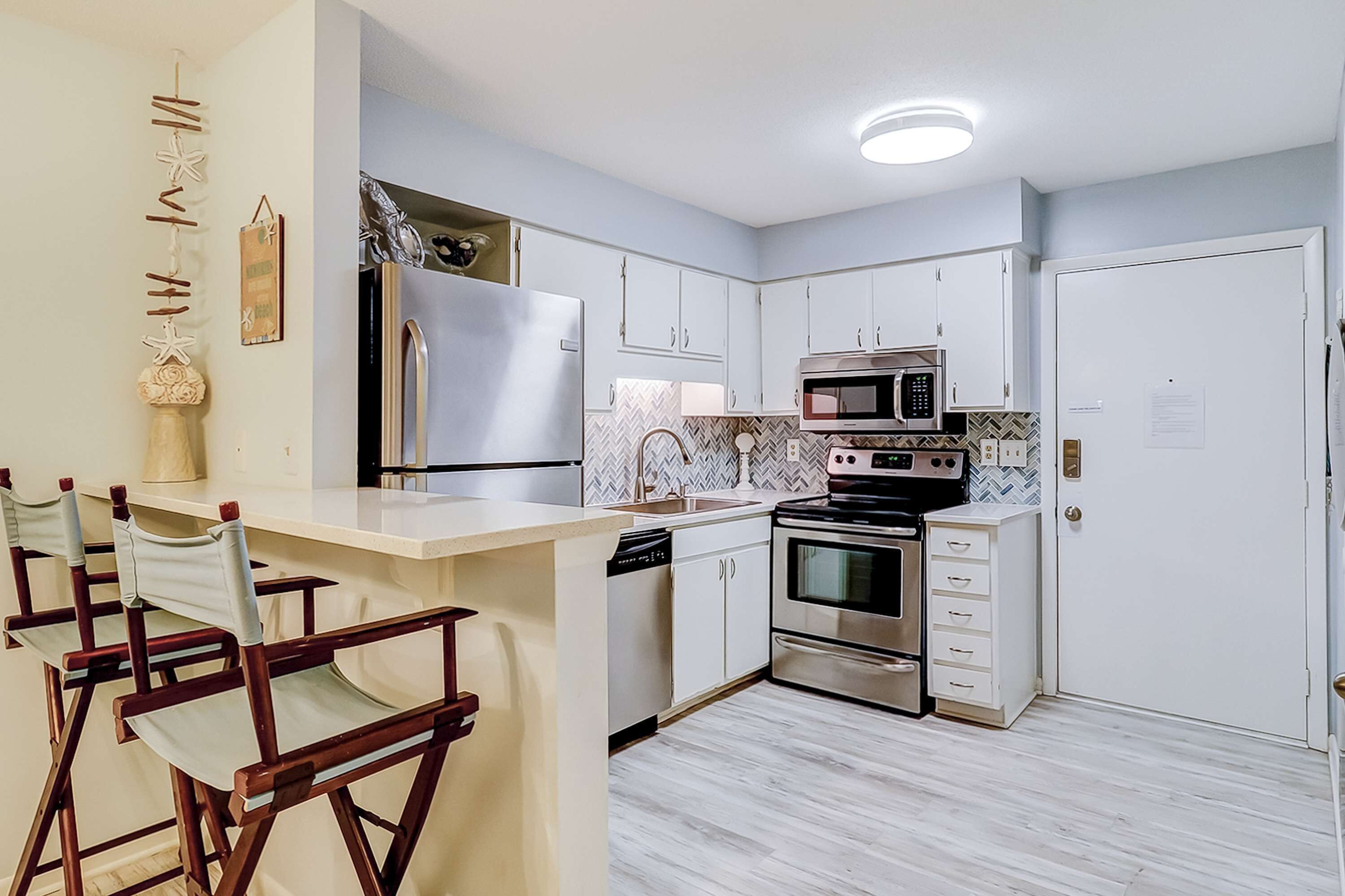 A modern kitchen with a central island, stainless steel appliances, and a herringbone tile backsplash.