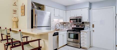A modern kitchen with a central island, stainless steel appliances, and a herringbone tile backsplash.