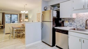 A modern kitchen with a refrigerator, dishwasher, and a herringbone tile backsplash. - Coastal Condo with Pool, Hot Tub, Tennis, Fast WiFi, AC, & WD, Near the Beach (Hilton Head)