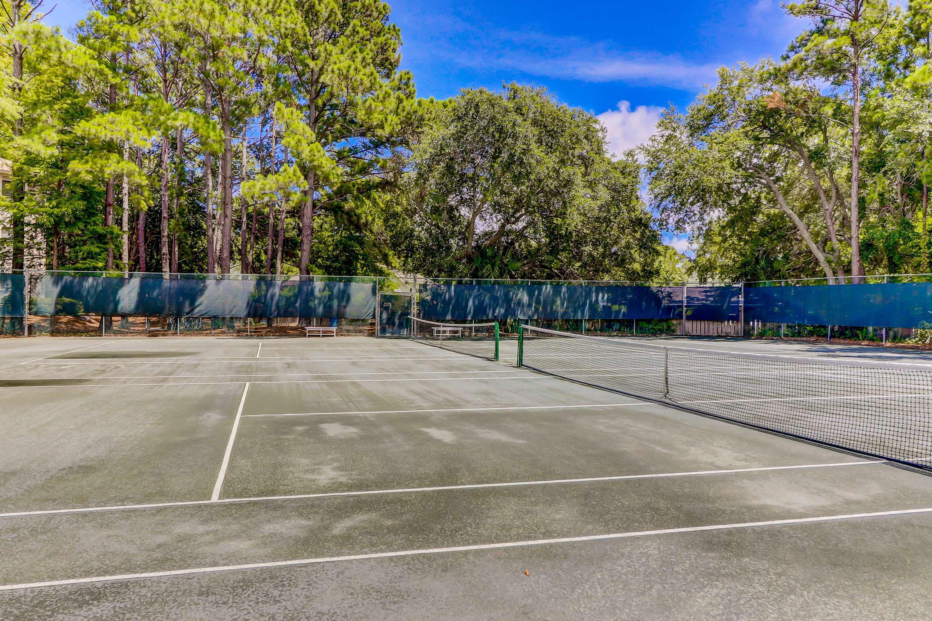 A tennis court with a net, surrounded by trees and a fence.