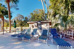 A poolside area with lounge chairs, a small building with a clock, and palm trees. - Charming third-floor condo- private balcony, shared pool, and steps to Coligny Plaza and the beach (Hilton Head)