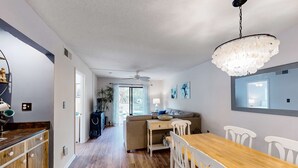 Moderni keittiö, jossa on puinen työtaso, ruokailutila puupöydällä ja valkoisilla tuoleilla, kattotuuletin ja suuri ikkuna.