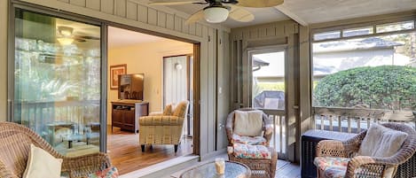 A covered outdoor area with wicker furniture, a ceiling fan, and a view of the interior.