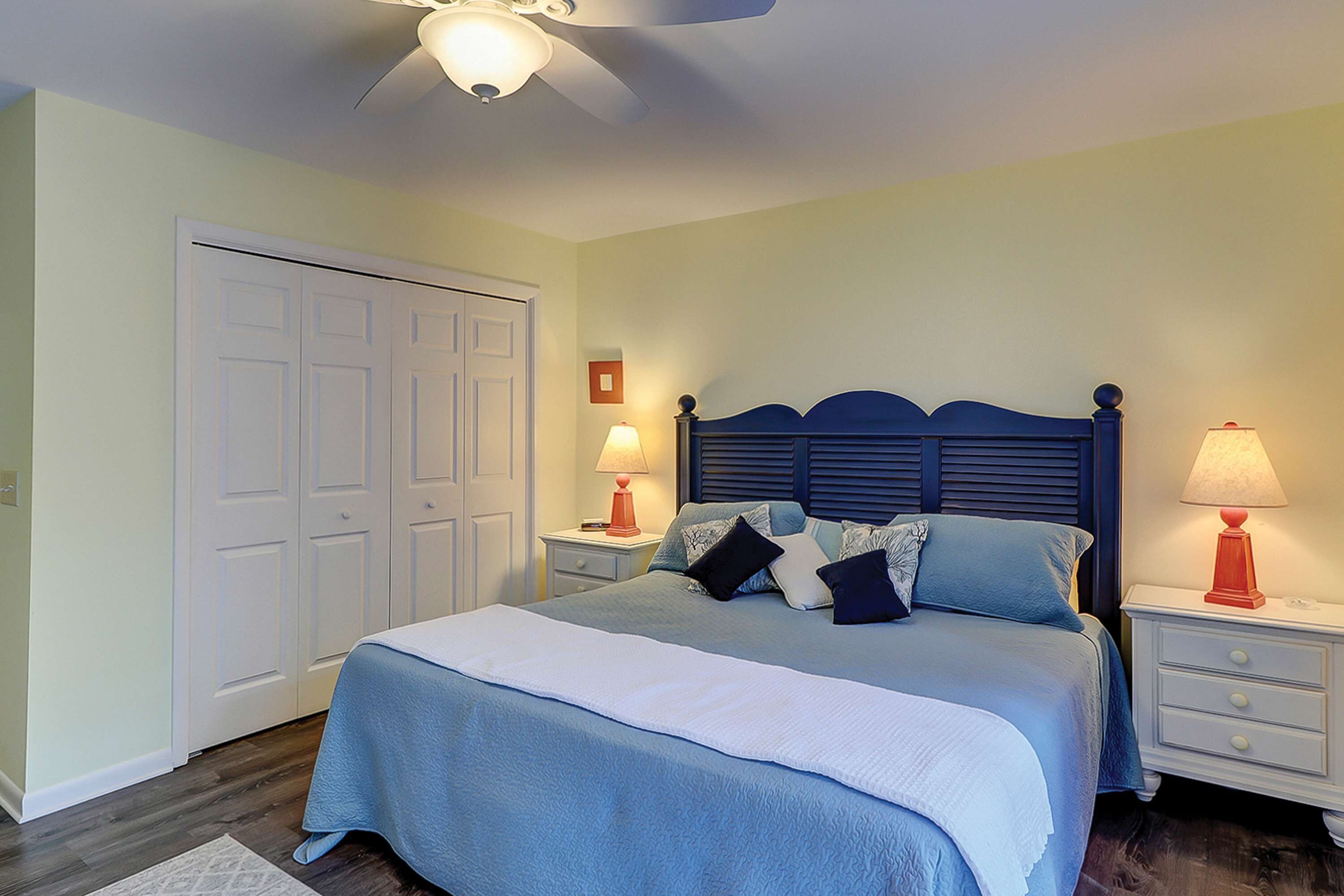 A bedroom with a bed, two bedside tables, a ceiling fan, and a door.
