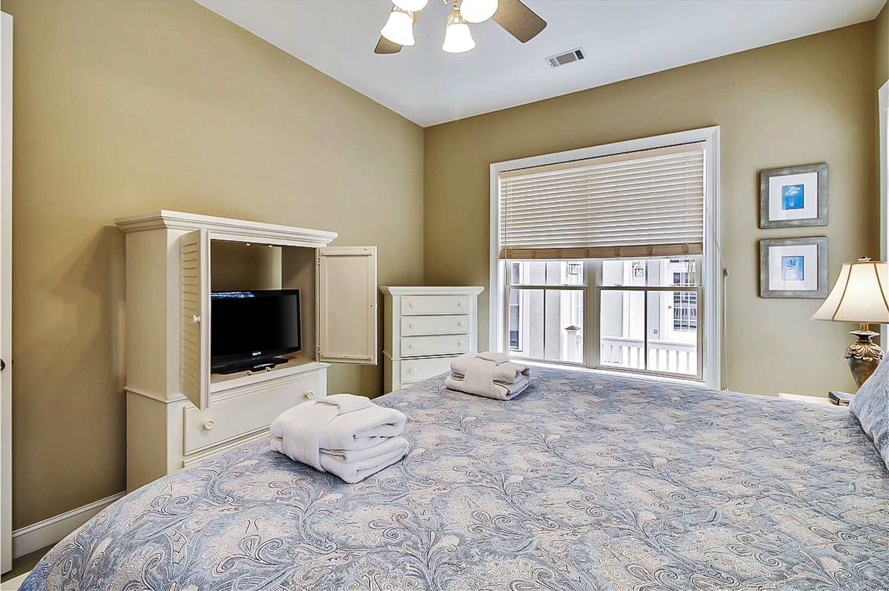 A bedroom with a bed, a television, a window with blinds, and a lamp.