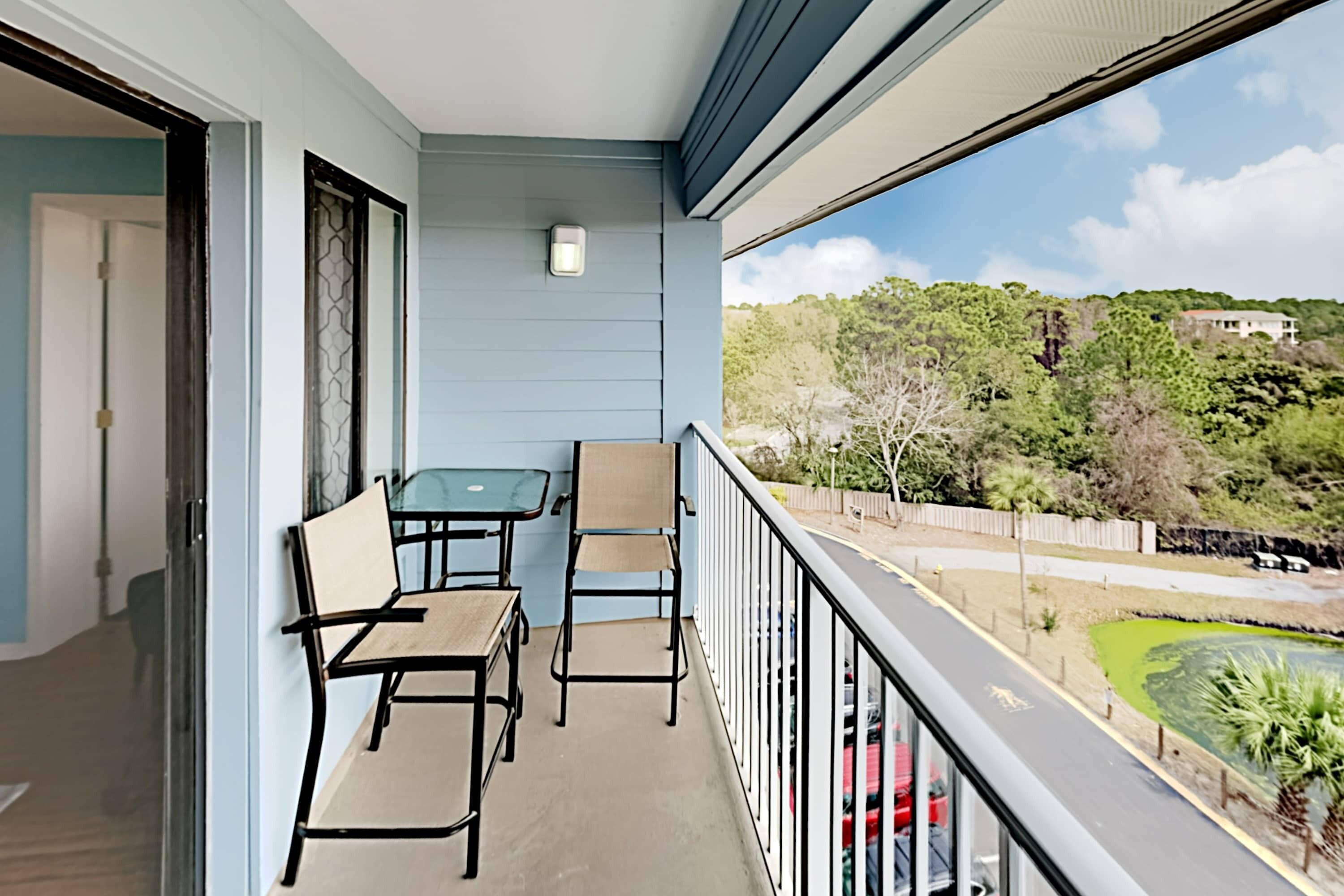A balcony with a table and chairs, a view of a road, and a building in the background.