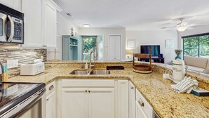 Una cucina moderna con mobili bianchi, piani di lavoro in granito, elettrodomestici in acciaio inossidabile e un'ampia finestra.