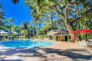 A swimming pool with lounge chairs and umbrellas, surrounded by trees and a building with a covered patio. - Lovely Condo w/ Shared Pool & Tennis - Dogs Welcome (Hilton Head)
