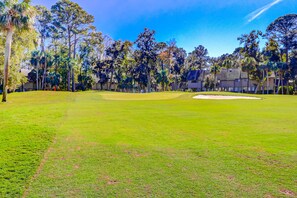 A golf course with a clear sky, trees, and a building in the background. - Lovely Condo w/ Shared Pool & Tennis - Dogs Welcome (Hilton Head)