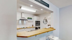 Eine moderne Küche mit einer Holzausziehtafel, weißen Schränken, einer Edelstahlspüle und einem kleinen Hocker.