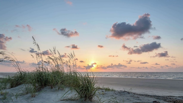Ein Strand mit Dünen, Gräsern, einem Sonnenuntergang und ruhiger See.