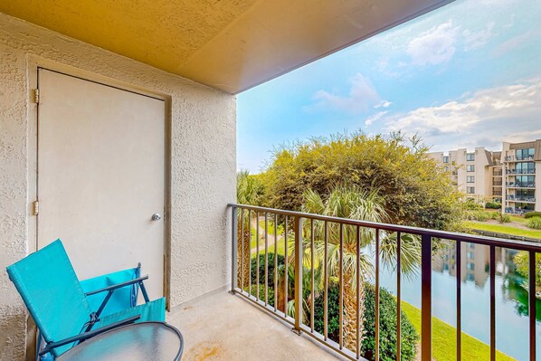 Ein Balkon mit einer Tür, einem blauen Stuhl und Blick auf ein Gebäude und Grünflächen.