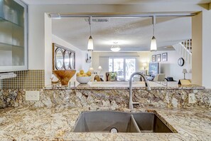 Cozinha com bancada de granito, pia de aço inoxidável, iluminação pendente e vista para a sala de estar.