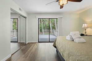 A hotel room with a bed, a nightstand, a lamp, a ceiling fan, and a sliding glass door leading to an outdoor deck. - Family-friendly condo w/ a furnished deck & shared pools - near golf & shops (Hilton Head)