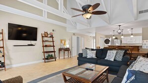 Ein geräumiges Wohnzimmer mit großem Fernseher, Deckenventilator und Essbereich mit Holztisch und -stühlen.