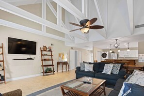 Ein geräumiges Wohnzimmer mit großem Fernseher, Deckenventilator und Essbereich mit Holztisch und -stühlen.