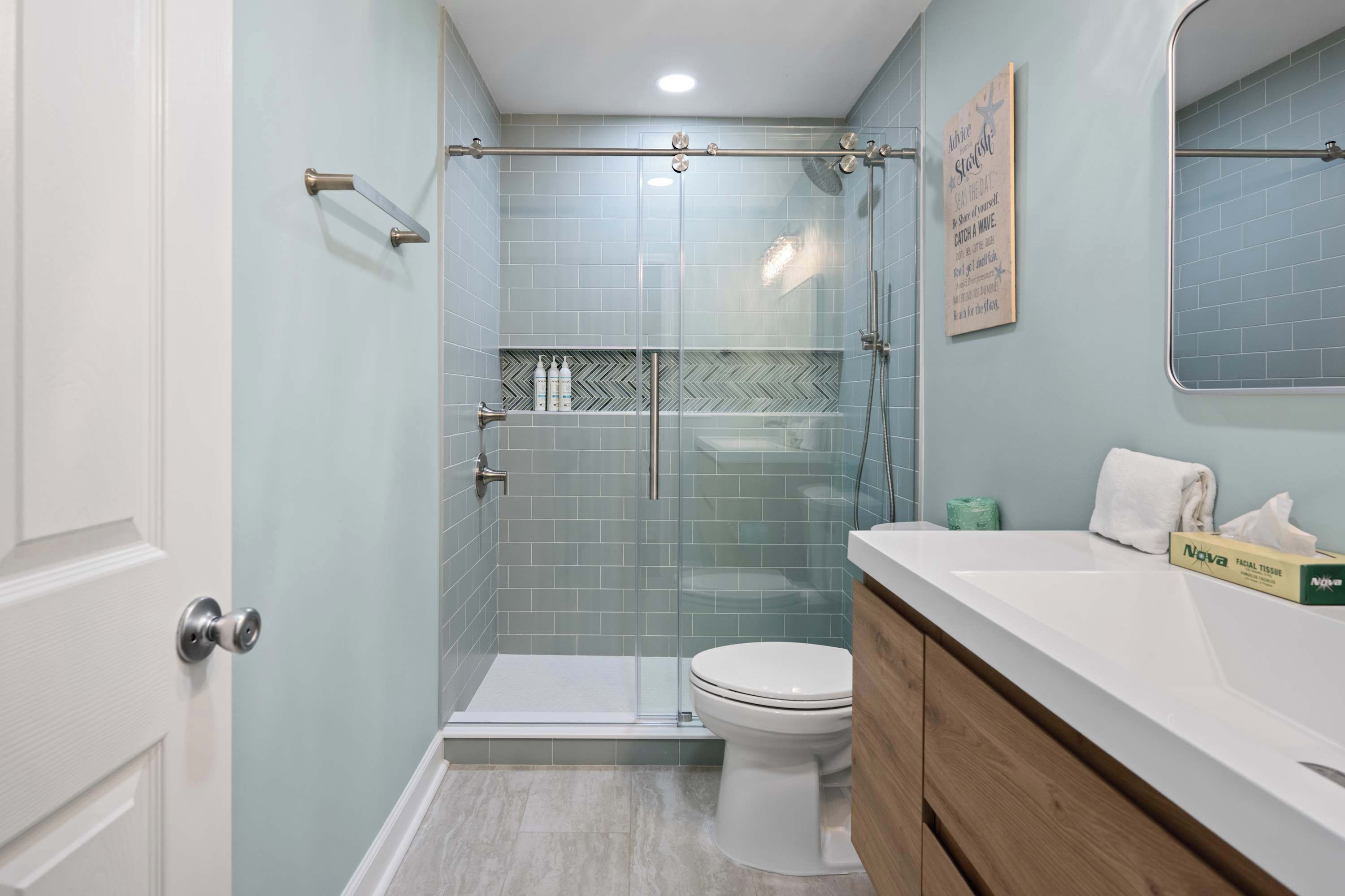 Un baño con cabina de ducha de vidrio, inodoro blanco, tocador con espejo y toallero de pared.