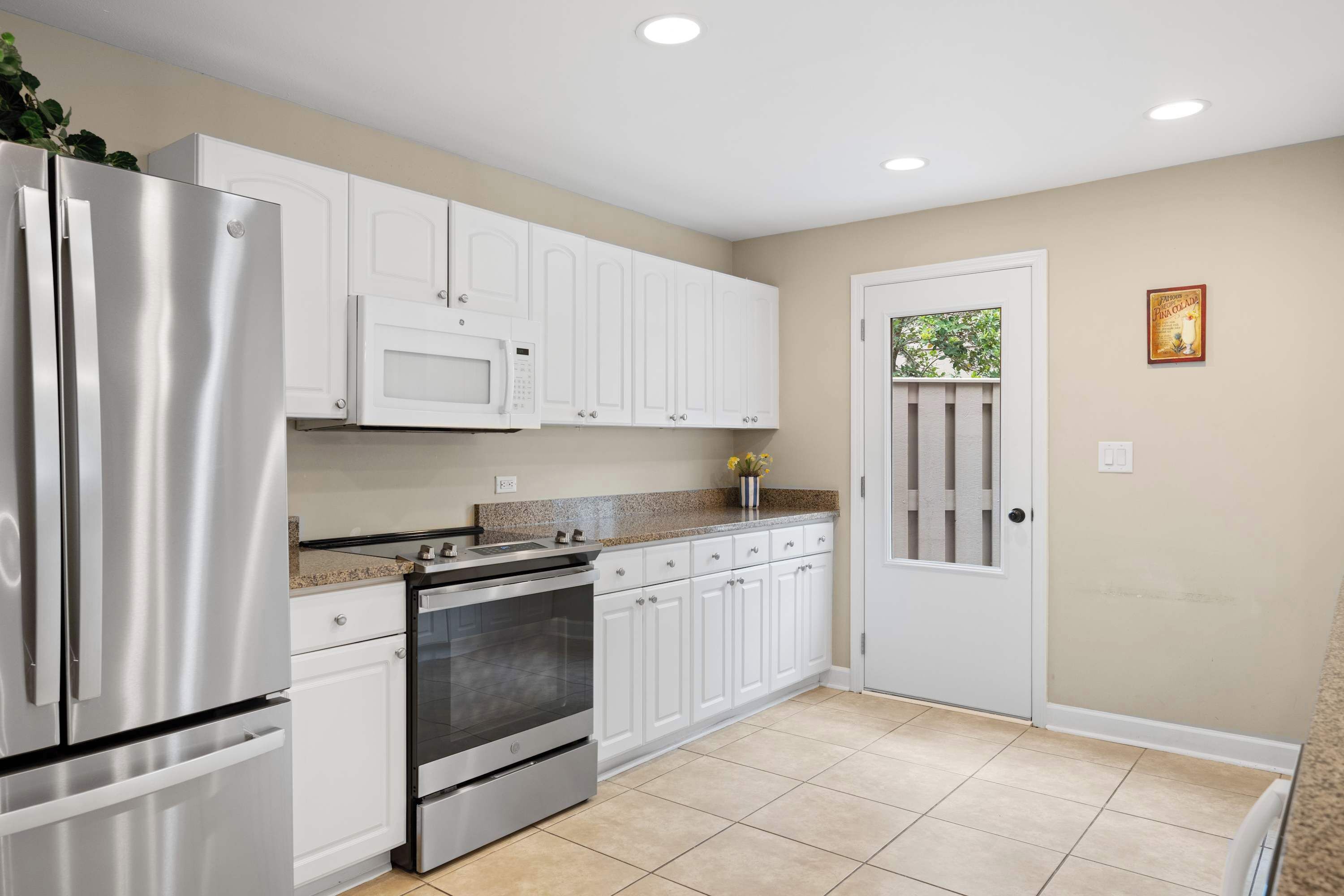 A kitchen with white cabinets, stainless steel appliances, a microwave, and a door with a window.
