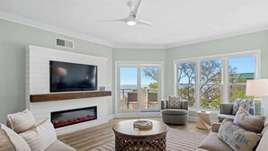 A living room with a fireplace, television, and a ceiling fan. - Coastal condo on the beach with panoramic views, beach access & a shared pool (Hilton Head)