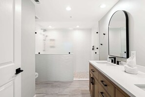 Une salle de bain moderne avec un meuble-lavabo blanc, un grand miroir et un espace douche.