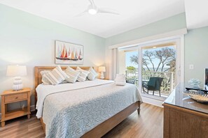 Une chambre à coucher comprenant un lit, des tables de chevet, un ventilateur de plafond, un tableau et un balcon avec une chaise.
