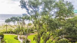 A lush green landscape with a pathway leading to a gazebo, overlooking a beach and ocean. - Coastal condo on the beach with panoramic views, beach access & a shared pool (Hilton Head)
