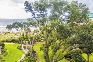 A lush green landscape with a pathway leading to a gazebo, overlooking a beach and ocean. - Coastal condo on the beach with panoramic views, beach access & a shared pool (Hilton Head)