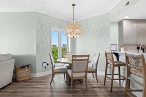 Un coin repas comprenant une table ronde, quatre chaises, un luminaire suspendu et un espace cuisine avec des placards.