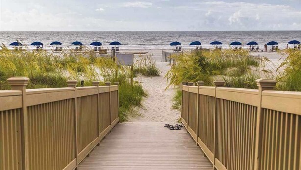 A wooden boardwalk leading to beach umbrellas and chairs. - Coastal condo on the beach with panoramic views, beach access & a shared pool (Hilton Head)