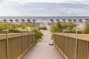Ein Holzsteg führt zu Strandstühlen und Sonnenschirmen.
