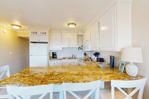 A kitchen with white cabinets, a granite countertop, and white chairs. - Coastal Condo with Shared Pool  Steps to the Beach, Walking Distance to Shopping and Dining (Hilton Head)