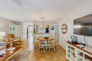 Un vaste espace de vie comprenant une table à manger, des chaises, un canapé, un téléviseur et une cuisine à l’arrière-plan.