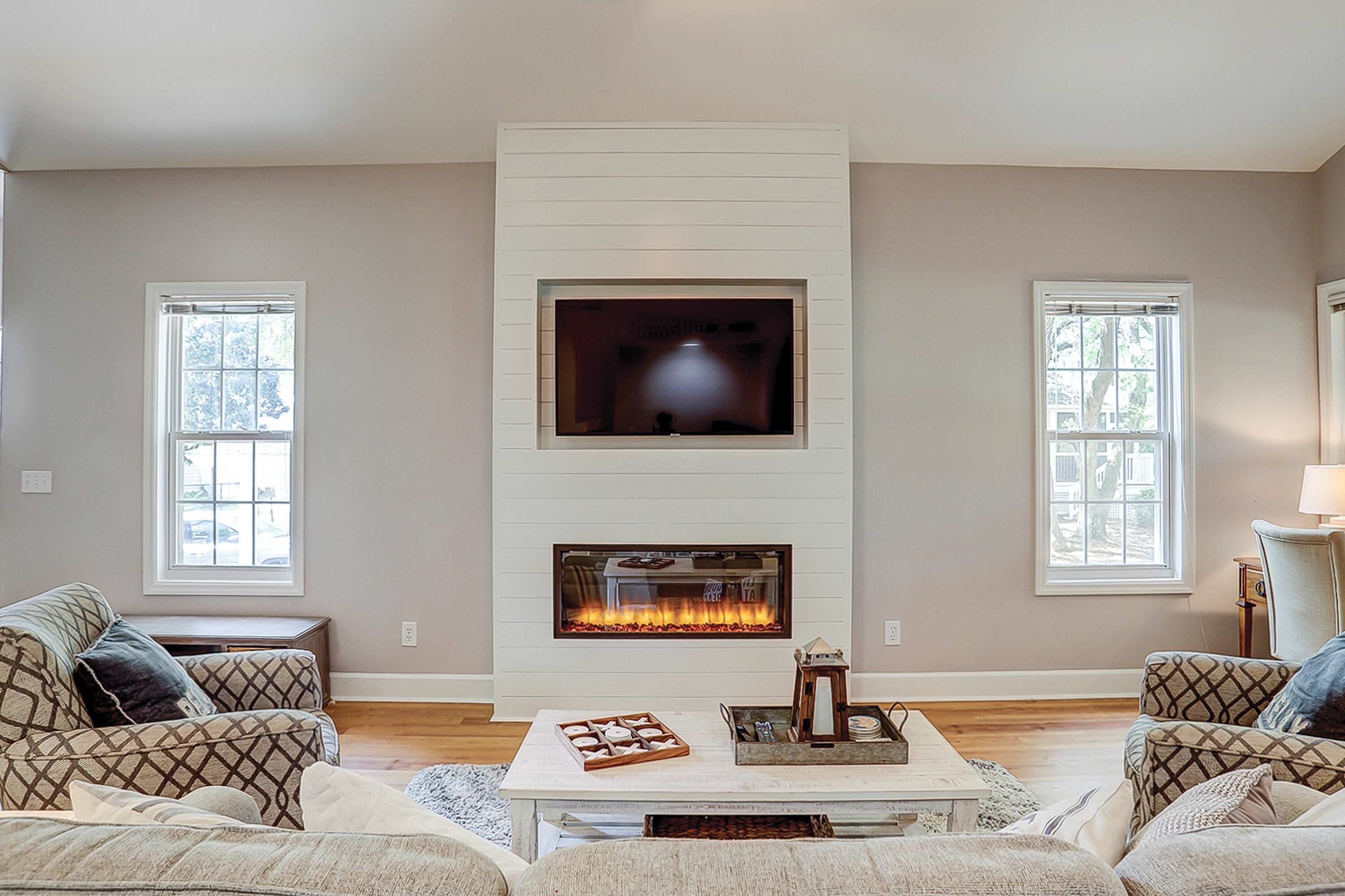 A living room with a fireplace, two sofas, a coffee table, and two windows.