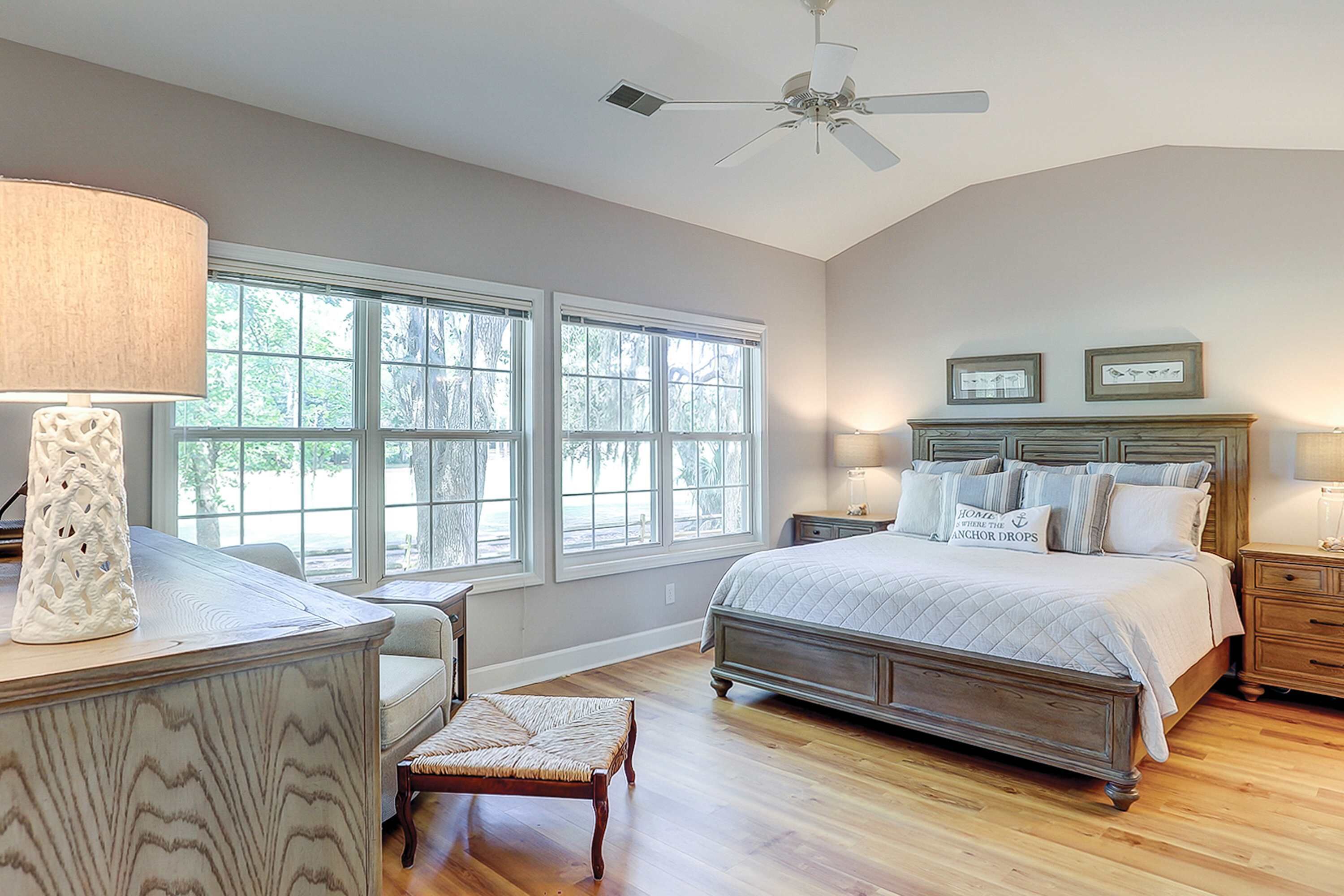 A bedroom with a bed, bedside tables, a desk, a chair, a window, and a ceiling fan.