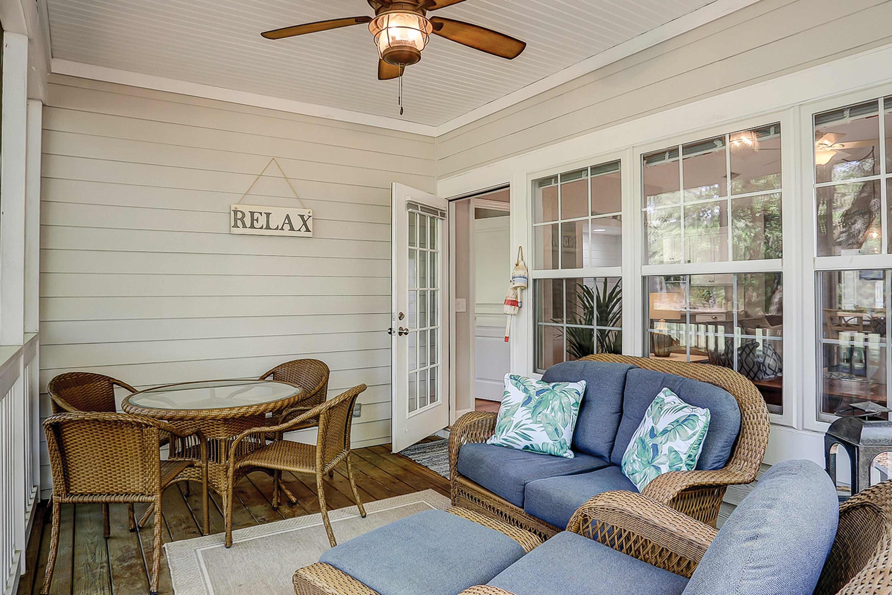 A covered porch with wicker furniture, a glass table, and a blue sofa with pillows.