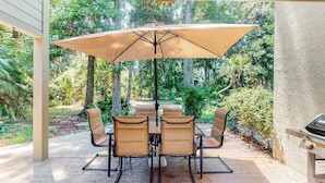 An outdoor patio with a table and chairs, an umbrella, and a grill. - Sailmaster Commons, Unit 16  Sun soaked villa with pool access and beach nearby (Hilton Head)