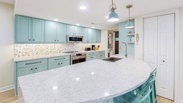 A kitchen with teal cabinets, a marble island, a microwave, and a sink. - Sailmaster Commons, Unit 16  Sun soaked villa with pool access and beach nearby (Hilton Head)