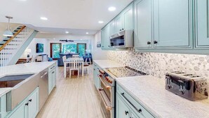 A modern kitchen with light blue cabinets, a stone backsplash, a built-in oven, and a toaster. - Sailmaster Commons, Unit 16  Sun soaked villa with pool access and beach nearby (Hilton Head)