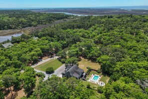 An aerial view of a property with a swimming pool, a large lawn, and dense forested areas.