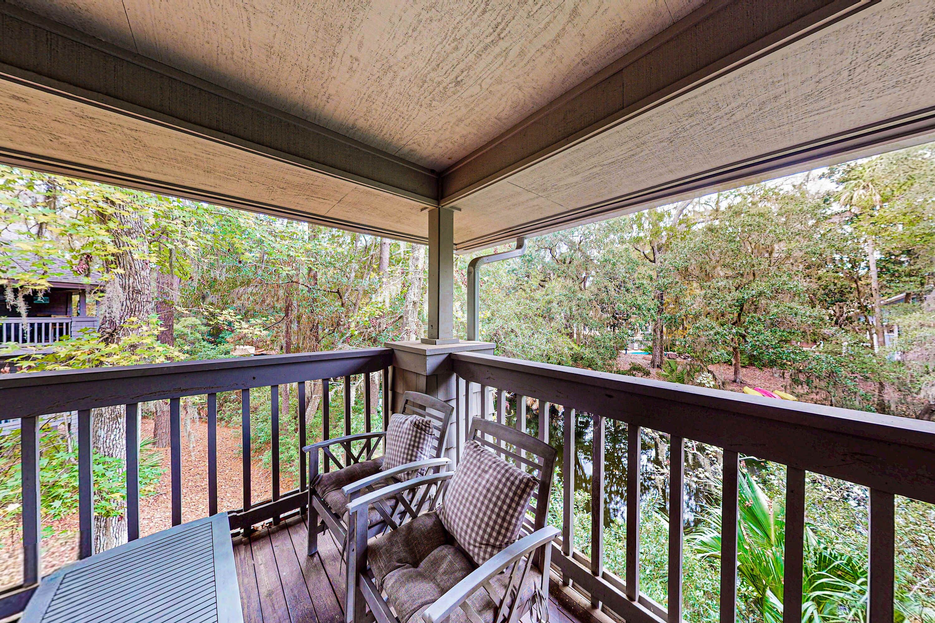 A covered porch with wooden railings, two rocking chairs, and a view of a wooded area.