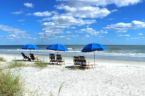 Ein Strand mit drei blauen Sonnenschirmen und Liegestühlen.