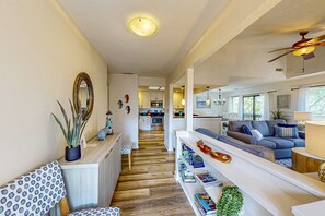 A modern living room with a sofa, bookshelves, and a dining area with a table and chairs. - Coastal resort condo with pool, tennis courts, beach access, golf, new deck (Hilton Head)