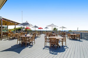 Una terraza de madera con mobiliario exterior, sombrillas y vista al océano.