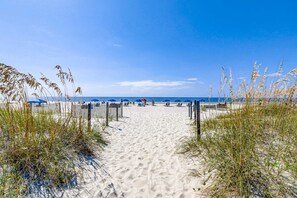 Uma trilha de areia que leva ao oceano, com guarda-sóis e cadeiras de praia.